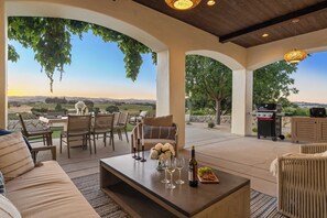 An outdoor patio with a sofa, dining table, and chairs, overlooking a scenic landscape. - Wine Country Escape w/ Views + Wine Cellar & Gym Caterina Dusi Vineyard by Avantstay (Paso Robles)