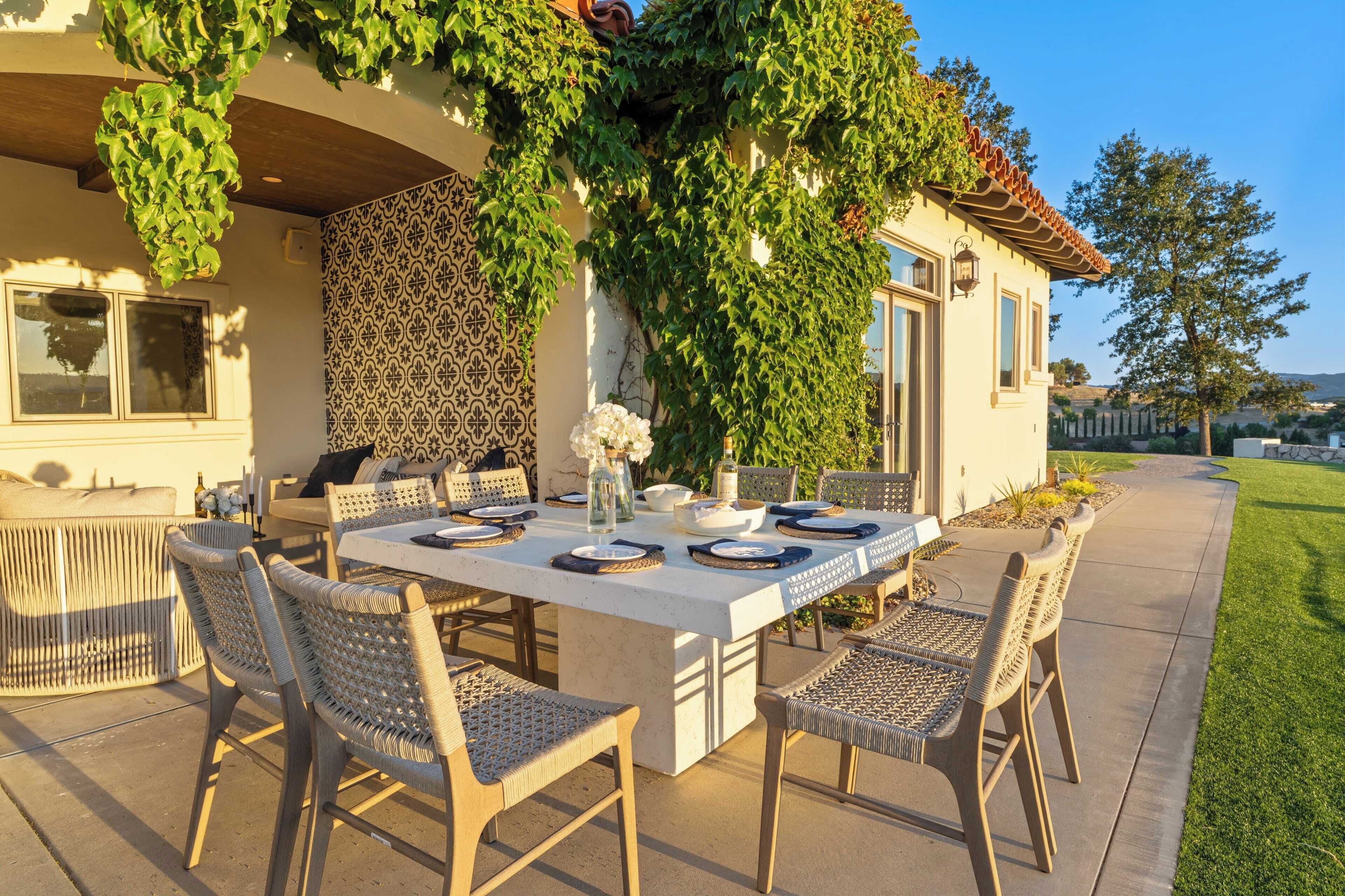 An outdoor dining area with a white table set for four, surrounded by wicker chairs.