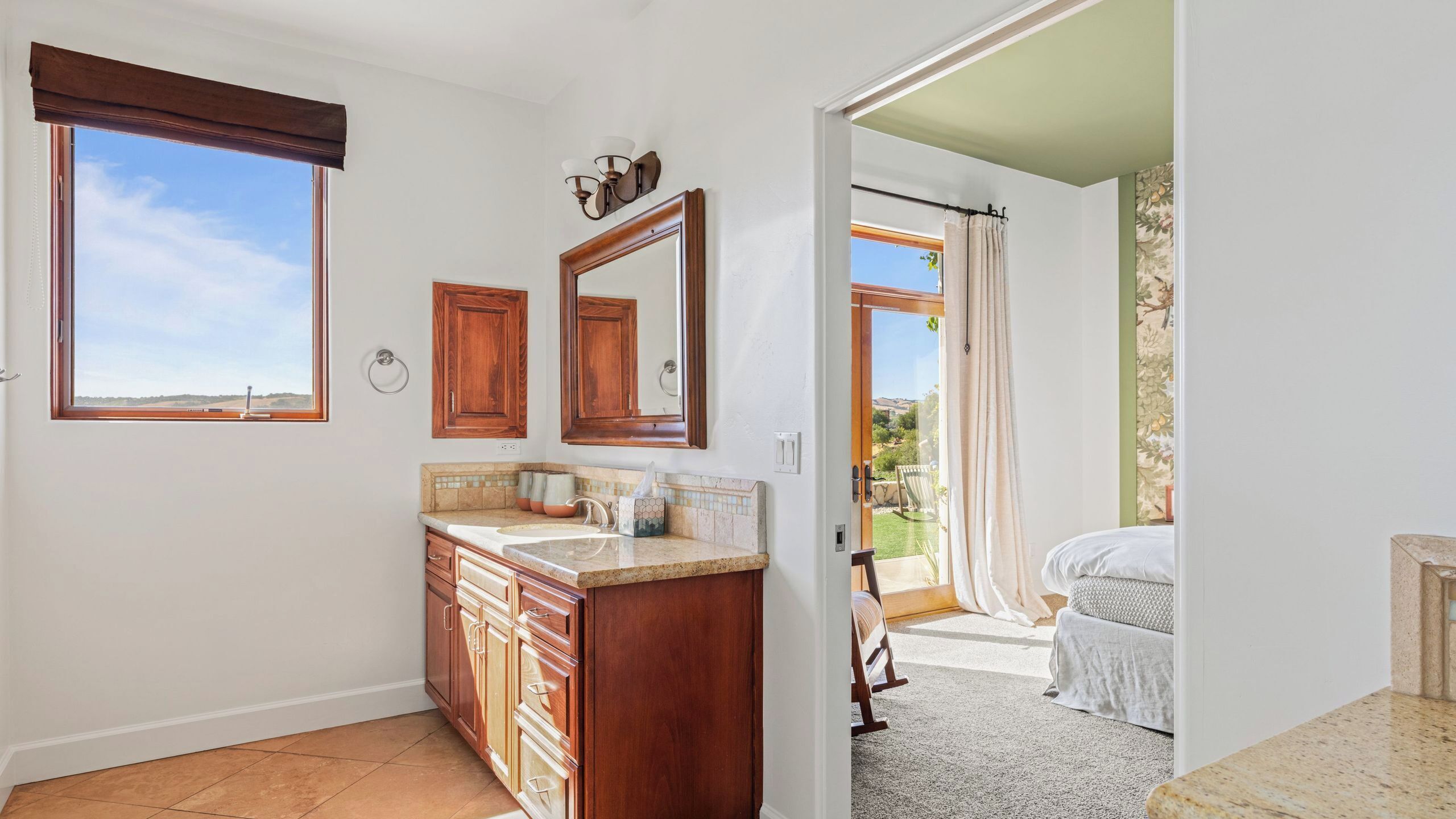 A bathroom with a wooden vanity, a large mirror, and a window.