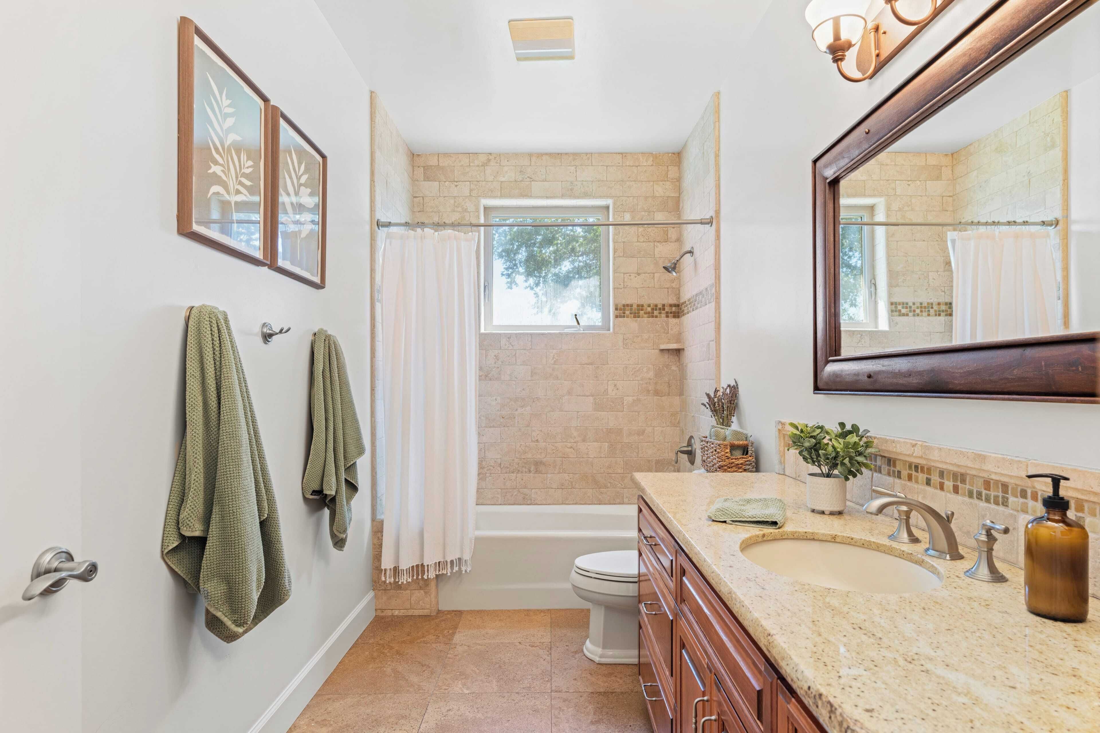 A bathroom with a bathtub, toilet, and sink. There are towels hanging on the wall and a window above the bathtub.