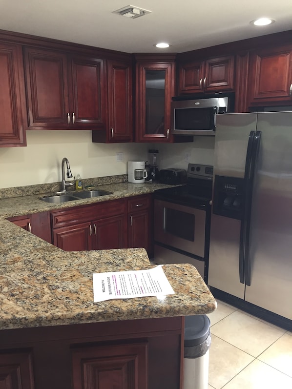 A kitchen with granite countertops, wooden cabinets, a stainless steel refrigerator, a microwave, and a coffee maker.