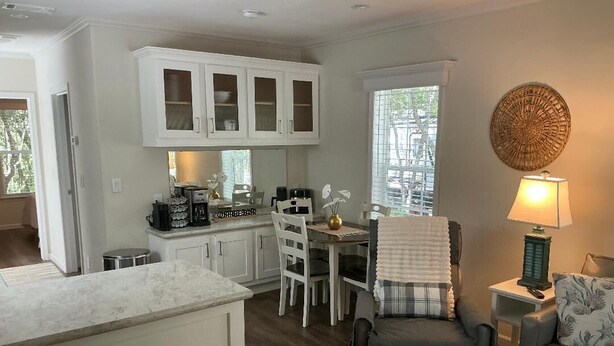 Une cuisine moderne avec des meubles blancs, un coin repas comprenant une table et des chaises, un fauteuil gris et une lampe sur une table d’appoint.