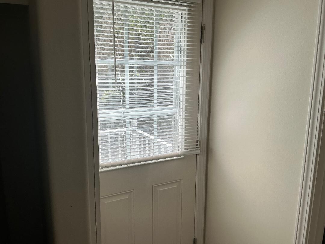 Eine weiße Tür mit Fenster und horizontalen Rollläden.
