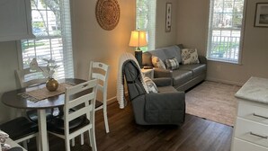 Un salon chaleureux avec un canapé gris, une table à manger avec des chaises, une lampe et un élément décoratif mural.