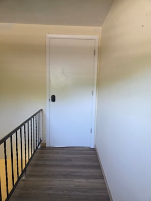Uma escada com piso de madeira e corrimão preto que leva a uma porta branca.