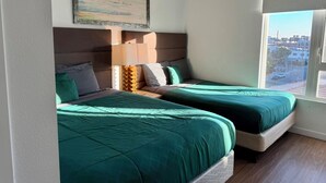 A room with two beds, a large window, and a painting on the wall.