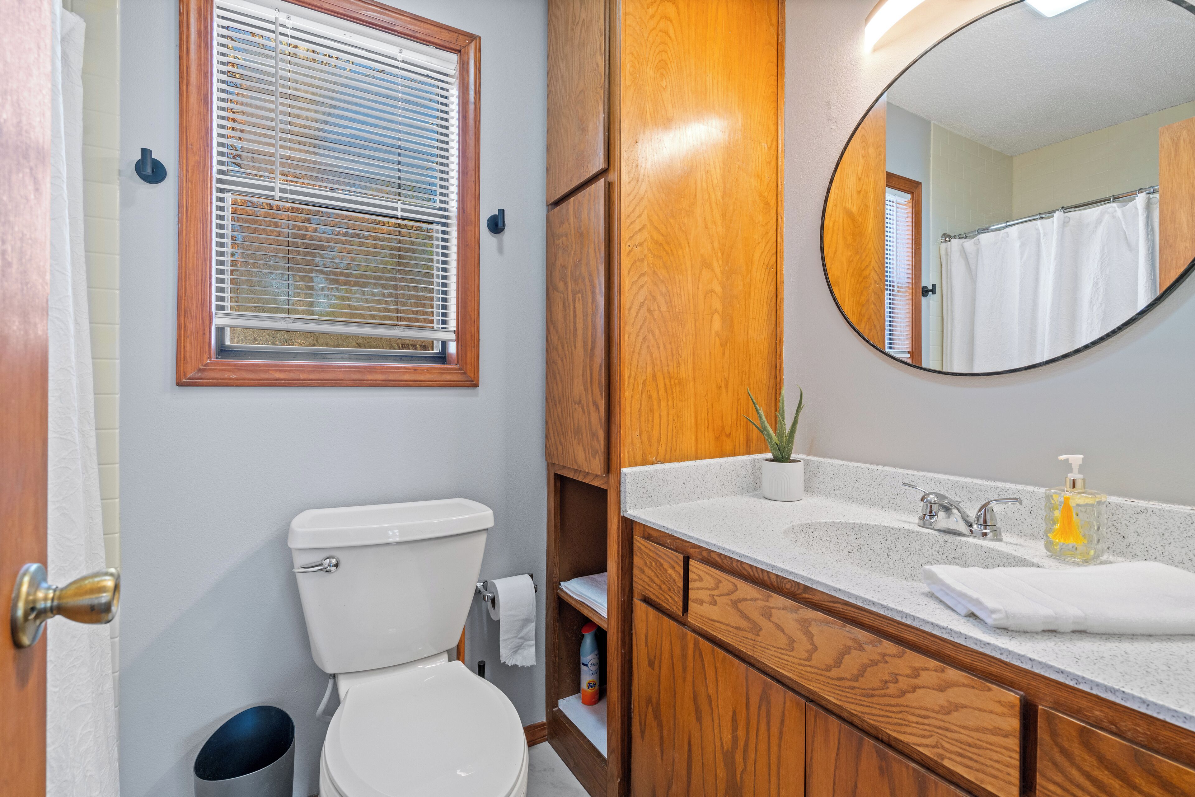 A bathroom with a toilet, sink, mirror, and window with blinds.