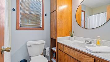 A bathroom with a toilet, sink, mirror, and window with blinds.