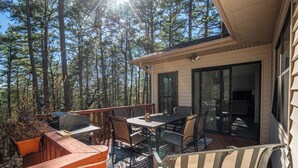 A deck with outdoor furniture, a grill, and a view of a forest. - Stay and Play HSV (Hot Springs)
