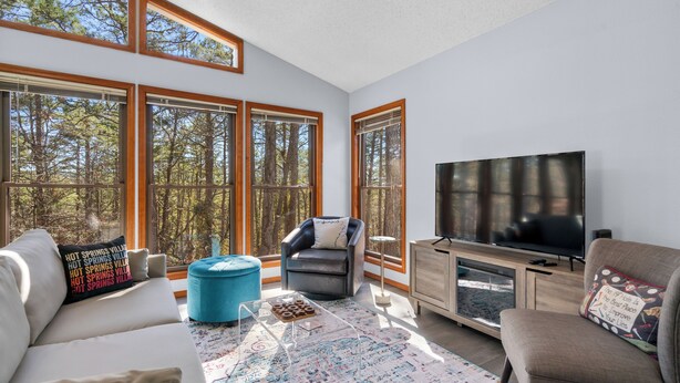 A spacious living room with large windows, a flat-screen TV, a sofa, a chair, and a coffee table. - Stay and Play HSV (Hot Springs)