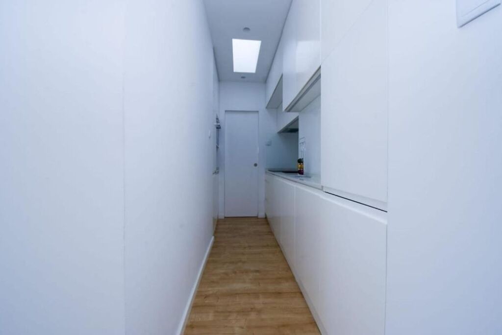 Un pasillo estrecho con paredes blancas y suelo de madera, que conduce a una puerta al final.