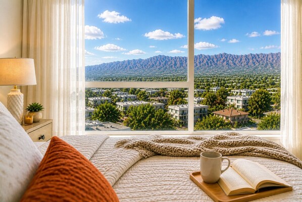 A bedroom with a large window, a bed, a bedside table with a lamp, and an open book.