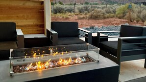 Une table avec foyer intégré, située dans un espace de détente extérieur moderne, offrant une vue sur un paysage désertique et des montagnes.