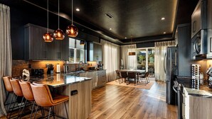 Une cuisine moderne dotée d’un îlot central, de tabourets de bar, d’appareils électroménagers en acier inoxydable et de luminaires suspendus.