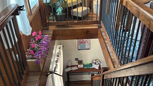 Una escalera de madera con barandilla metálica que conduce a un rellano en el segundo piso, con vista a una chimenea y una mesa con objetos encima.