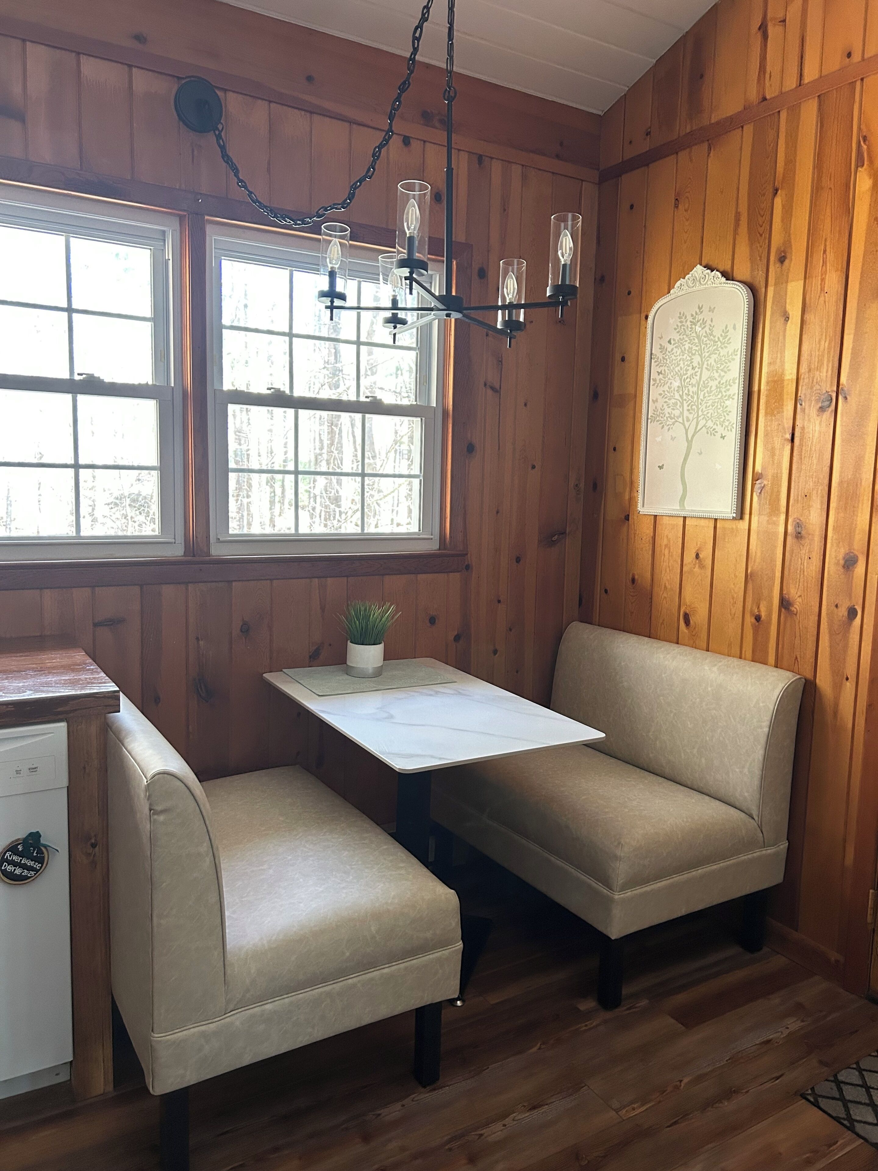 A cozy room with wooden walls, a white table, two beige sofas, a small potted plant, and a wall-mounted decorative piece.
