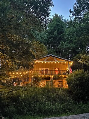 A wooden cabin with a balcony, surrounded by dense trees. - Fall for River Breeze: River Front Cabin, River Access, Fenced Yard, Dogs...YES! (West Jefferson)