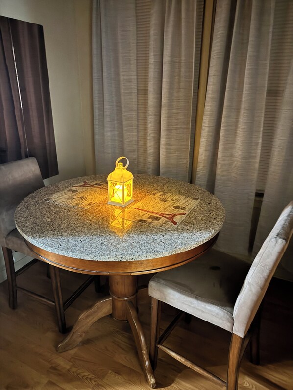 A round table with a granite top, surrounded by wooden chairs, and a lit lantern in the center.
