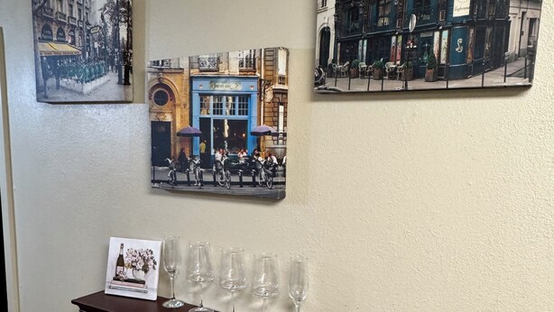 Una pared con tres cuadros de edificios y una repisa con copas de vino.