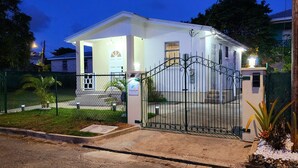 Una casa de dos pisos amb entrada tancada per reixa, un petit porxo i exterior ben il·luminat.