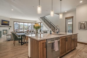 Une cuisine moderne dotée d’un îlot central, de meubles en bois, de luminaires suspendus, d’un escalier et d’un coin repas offrant une vue agréable.