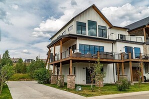 A modern two-story house with a balcony, stone pillars, and a driveway.