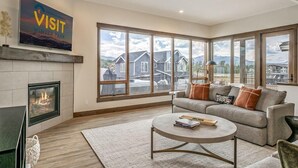 A modern living room with a fireplace, large windows, a sofa, and a coffee table. - Brand-New 4BR Townhome | Private Hot Tub (Fraser)