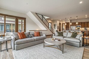 A spacious living area with a grey sofa, a coffee table, and a staircase leading to an upper level.