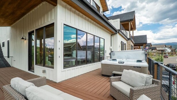 A deck with outdoor furniture, a hot tub, and large windows overlooking a residential area. - Brand-New 4BR Townhome | Private Hot Tub (Fraser)
