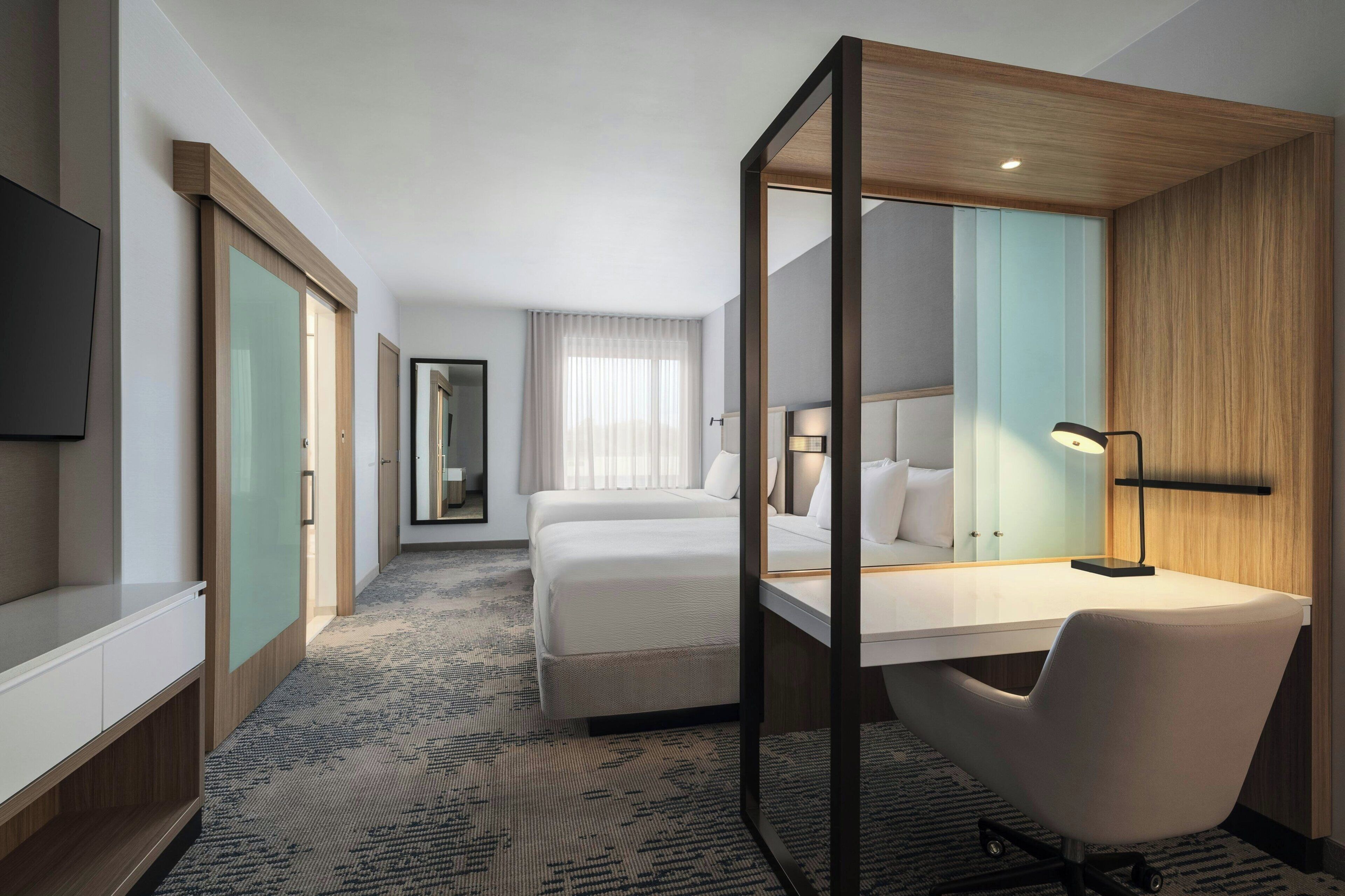 A hotel room with a bed, a desk, a chair, a TV, and a mirror.
