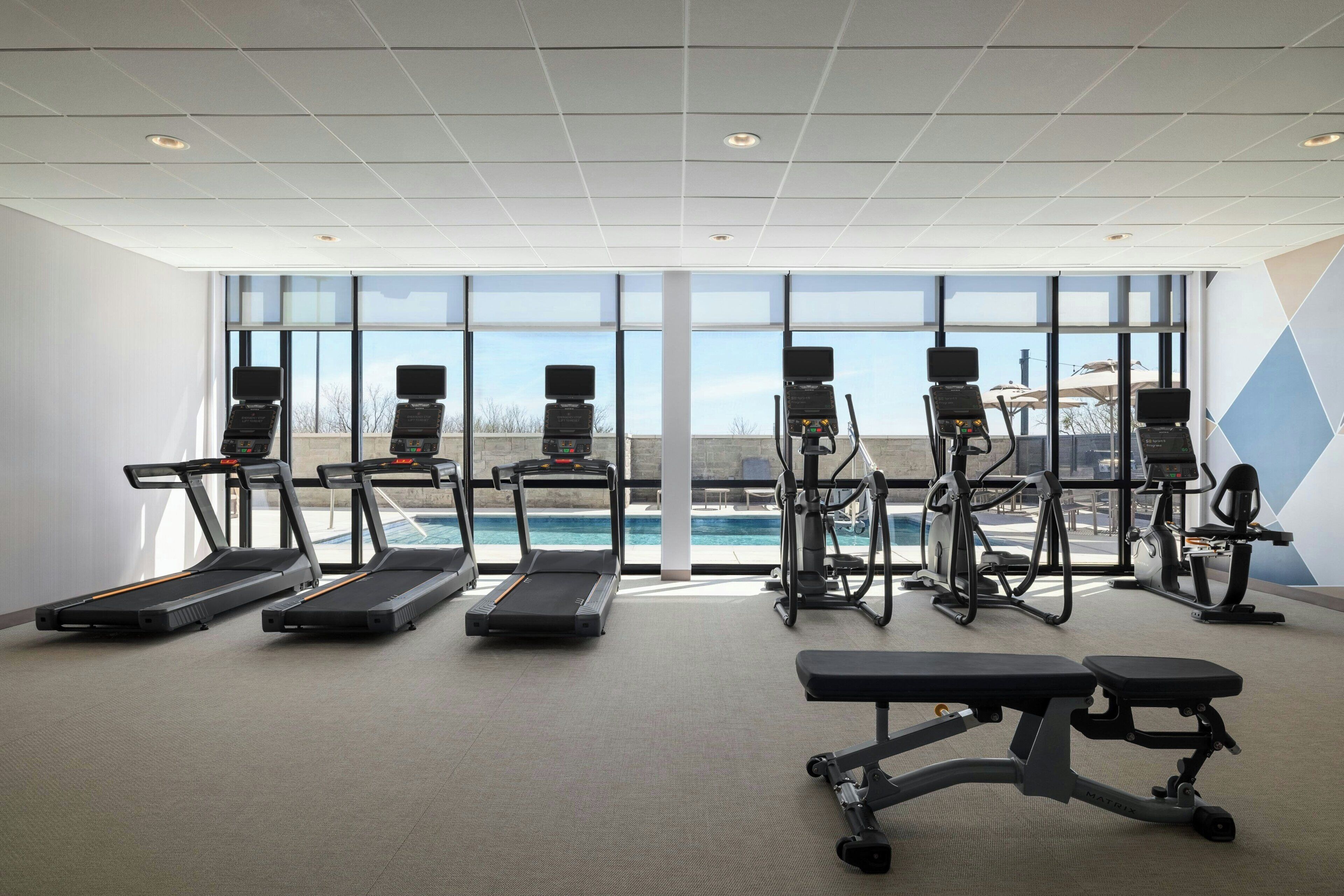 A gym with treadmills, elliptical machines, and a bench.