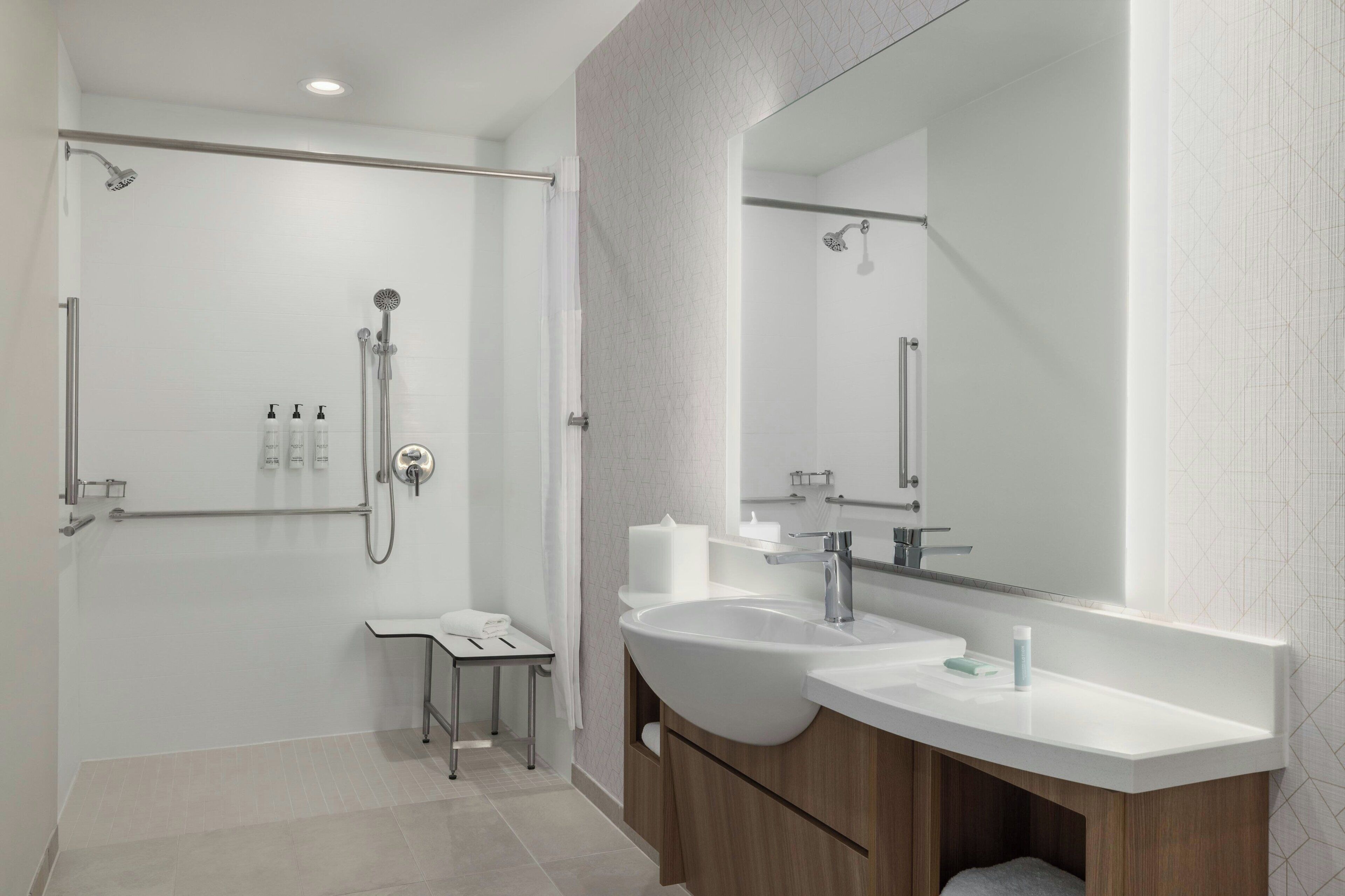 Un bany modern amb plat de dutxa, un lavabo amb un mirall gran i un vàter.