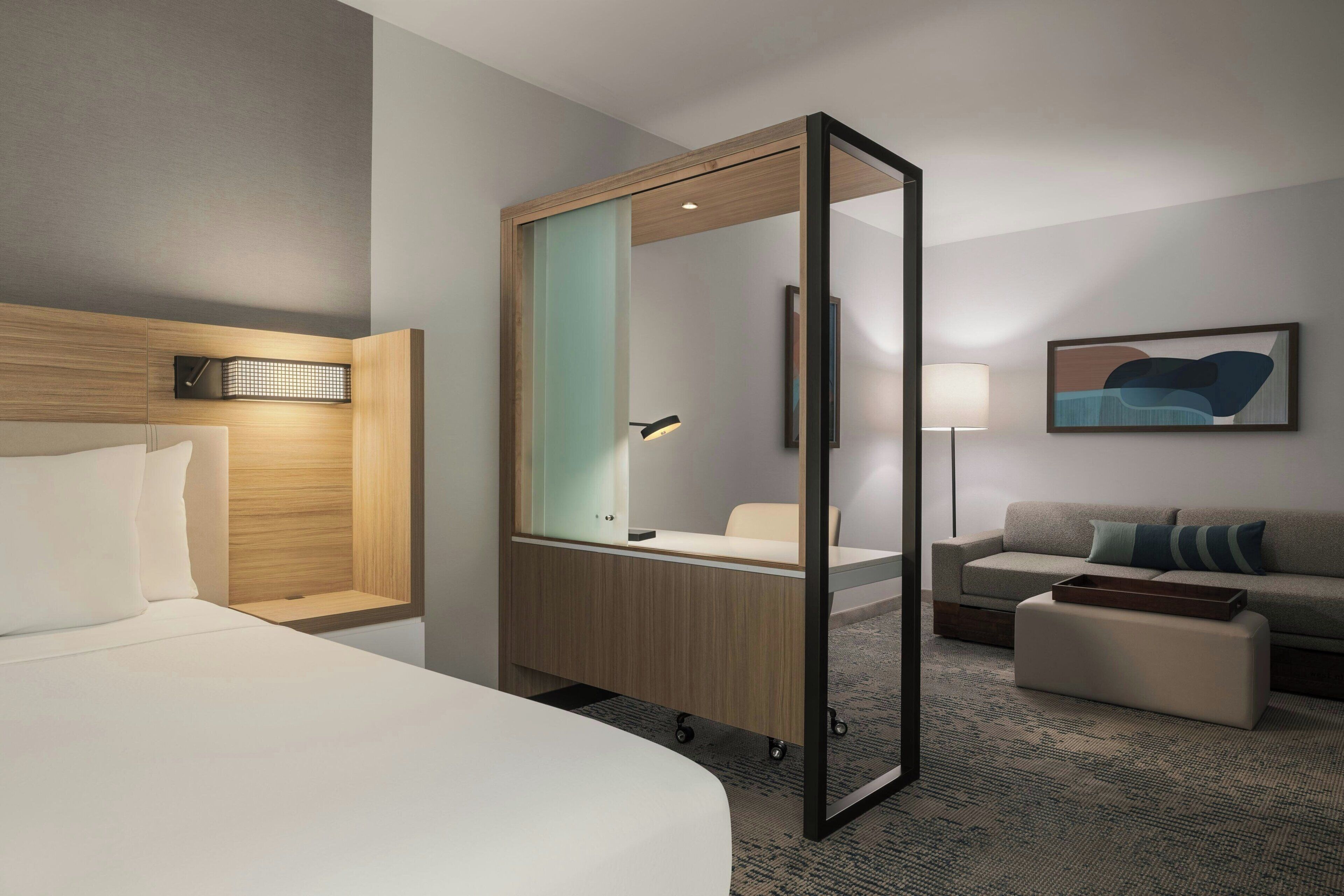 A hotel room with a bed, a desk with a chair, a sofa, and a large mirror.
