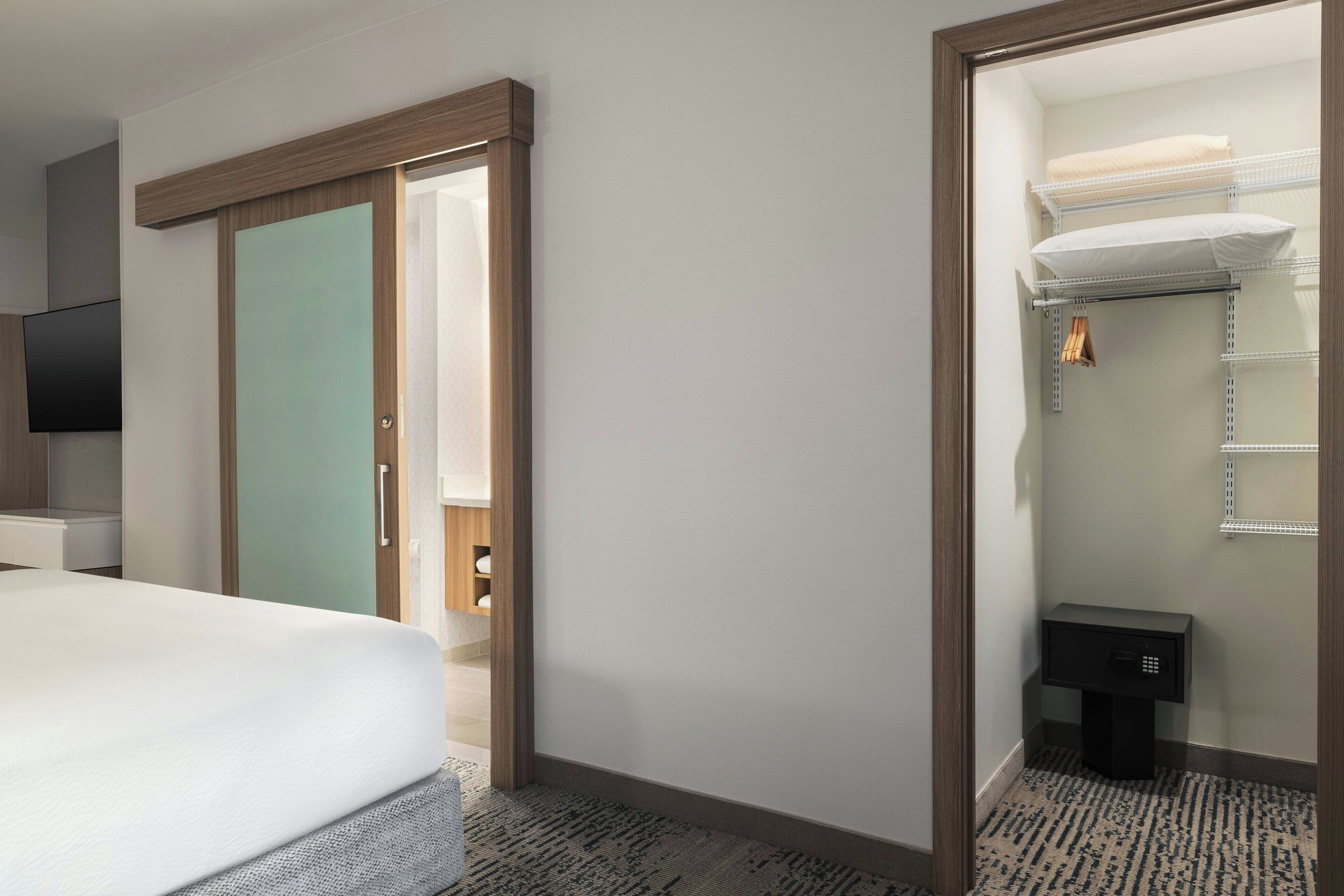 A hotel room with a bed, a television, a wardrobe, and a bathroom with a shelf and towel rack.