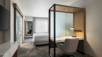 A hotel room with a bed, a desk, a chair, a TV, and a mirror.