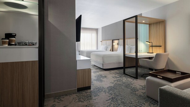 Quarto de hotel moderno com cama, escrivaninha, cadeira, televisão e comodidades para café.