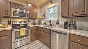A modern kitchen with stainless steel appliances, wooden cabinets, granite countertops, and a window providing natural light. - Cozy Mountainside Studio Nestled in the Trees (Sylva)