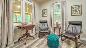A room with two leather chairs, a wooden table, a teal ottoman, and two windows with curtains. - Cozy Mountainside Studio Nestled in the Trees (Sylva)