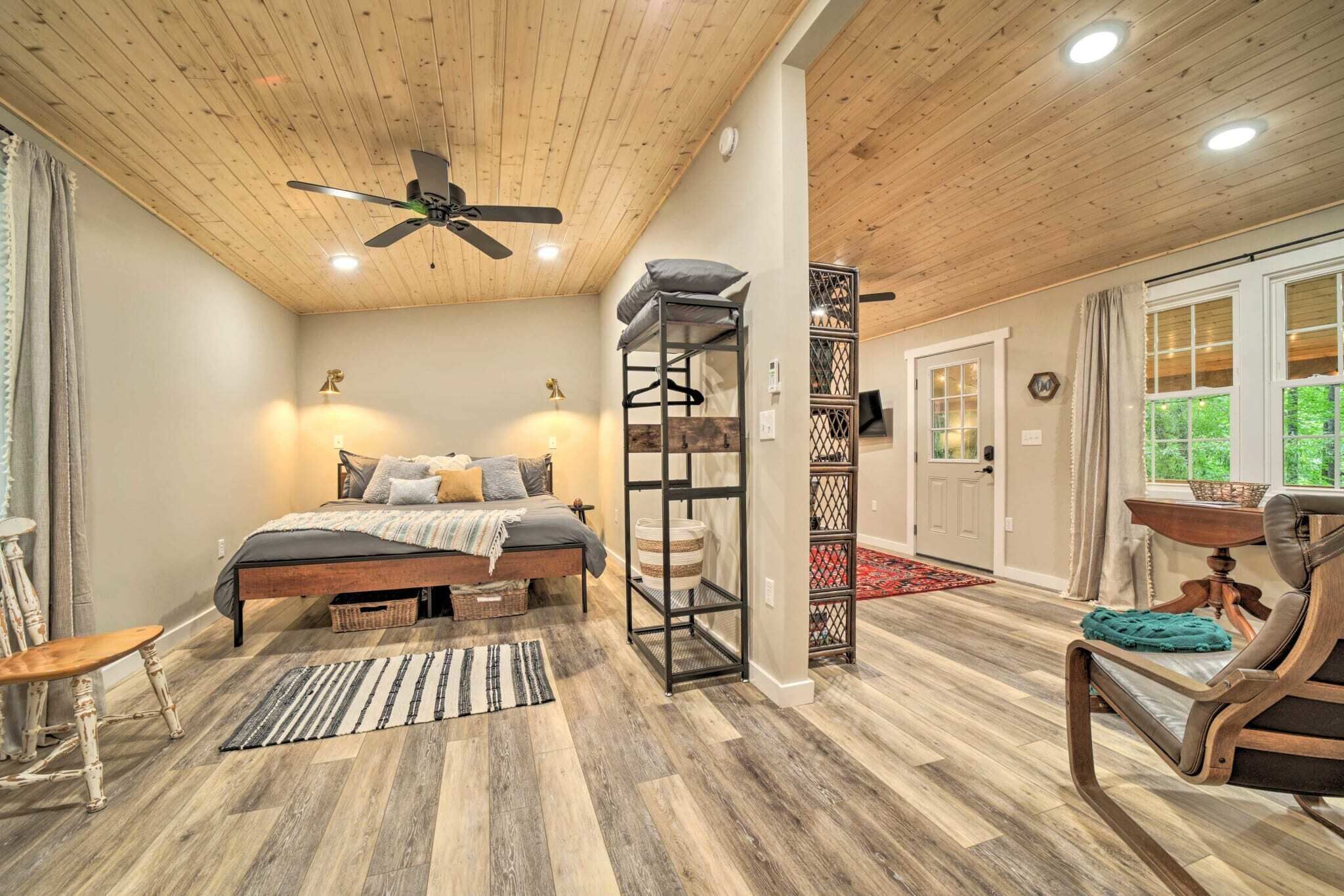 A bedroom with a bed, a ceiling fan, a wooden floor, a window, and a door.