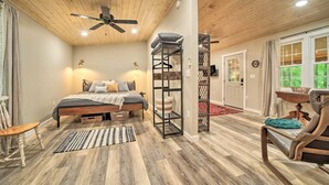 A bedroom with a bed, a ceiling fan, a wooden floor, a window, and a door. - Cozy Mountainside Studio Nestled in the Trees (Sylva)