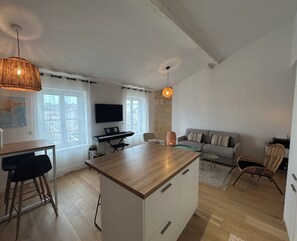A modern living space with a kitchen island, a dining area, a sofa, and a TV mounted on the wall.