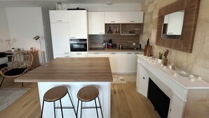 Et moderne køkken med hvide skabe, en træø med to barstole, indbygget ovn og en stenvæg.