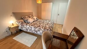 Et soveværelse med seng, sengebord, lampe, stol, skrivebord og skab.