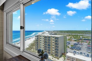A view from a window overlooking a beach, a parking lot, and a hotel building. - Pinnacle Port A725 | Indoor & Outdoor Pools | On-Site Dining | My Beach Getaways (Panama City Beach)