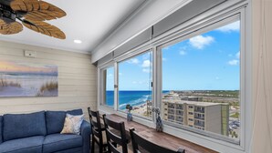 A room with a view of the ocean, a sofa, a dining table with chairs, and a ceiling fan.