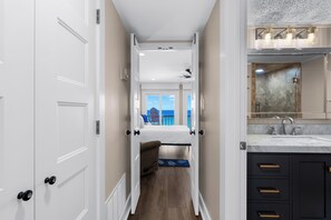 A narrow hallway leading to a bedroom with a bed, a ceiling fan, and a view of the ocean.