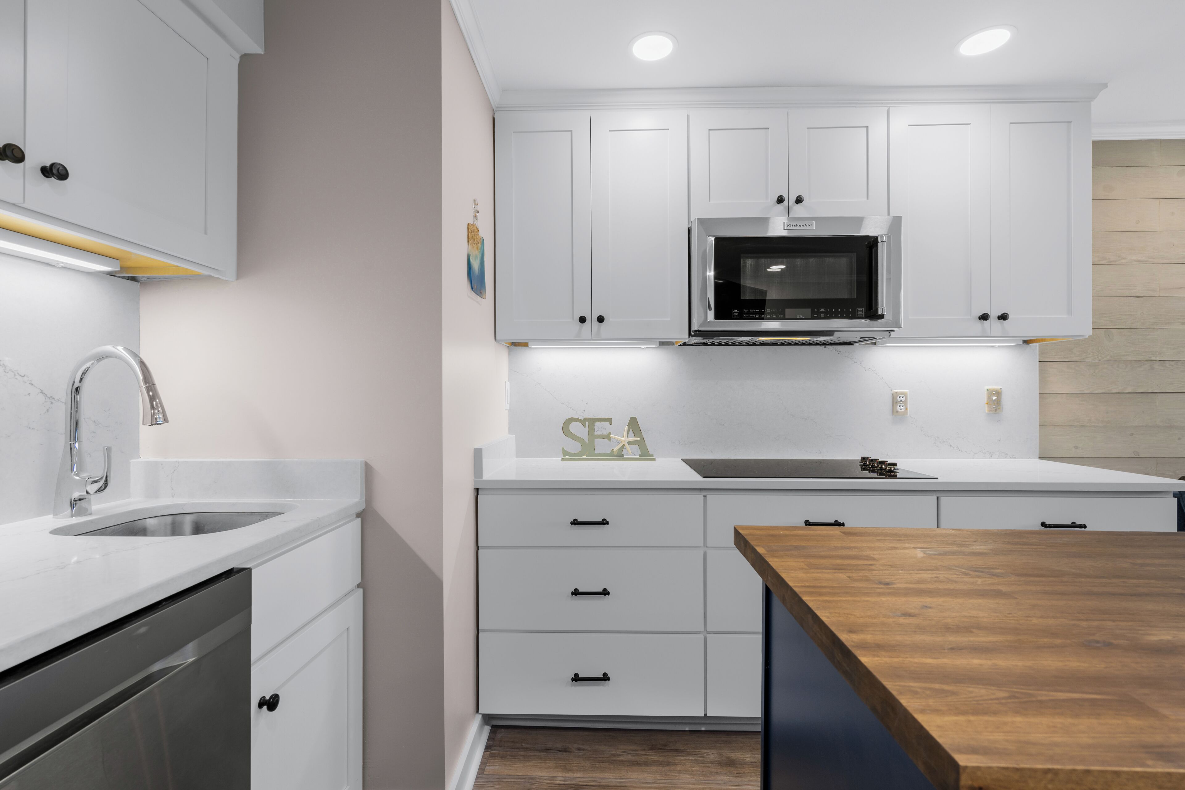 A modern kitchen with white cabinets, a stainless steel sink, a built-in microwave, and a wooden countertop.