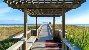 A wooden boardwalk leading to a beach with a pergola structure. - Beautiful Spanish Key #101 | Steps from Flora Bama | Oceanfront Condo | My Beach Getaways (Pensacola)