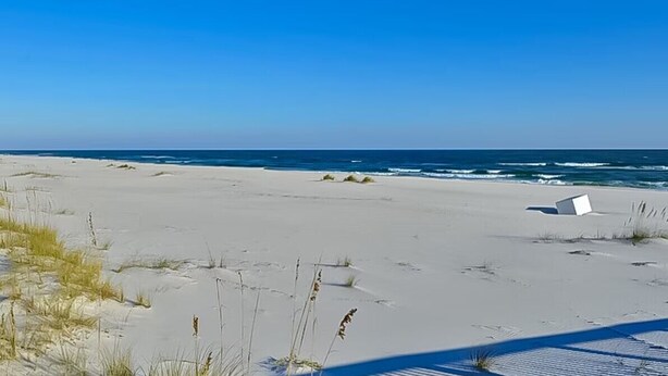 A sandy beach with a white structure, possibly a lifeguard tower, and the ocean in the background. - Beautiful Spanish Key #101 | Steps from Flora Bama | Oceanfront Condo | My Beach Getaways (Pensacola)