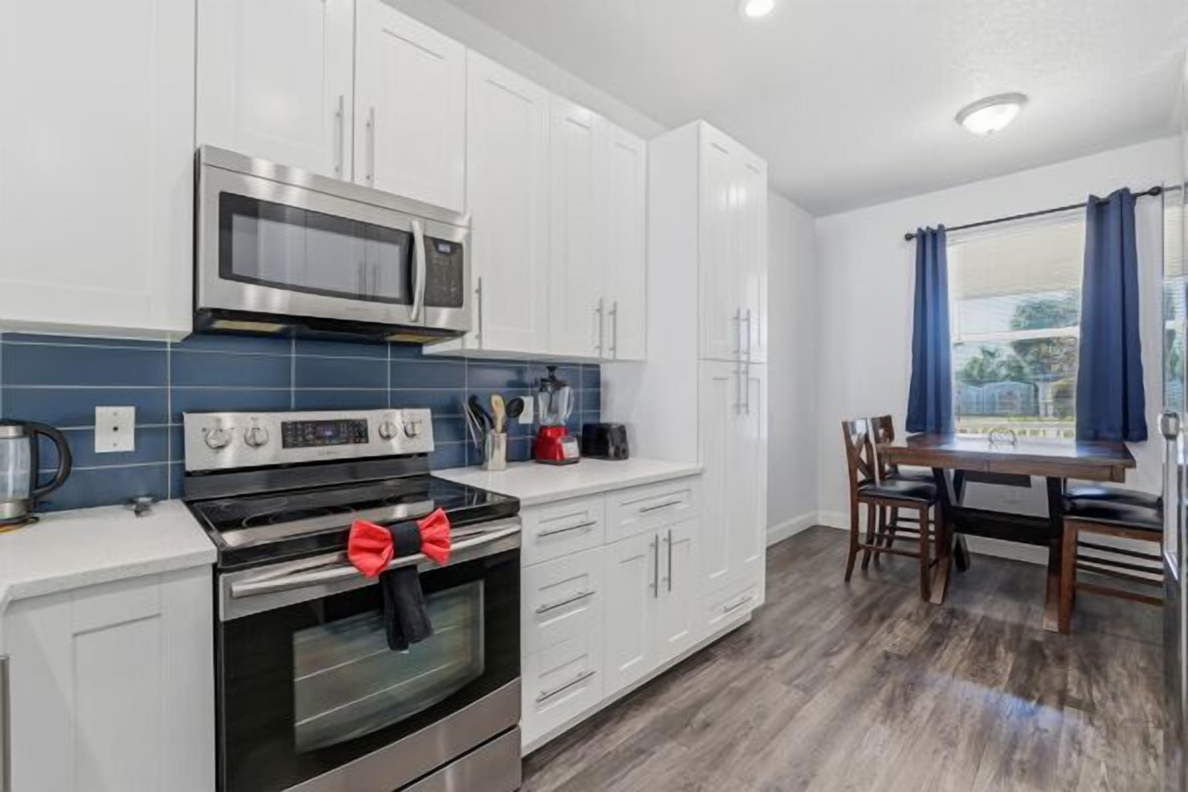 A modern kitchen with white cabinets, a stainless steel oven, a microwave, and a dining area with a table and chairs.